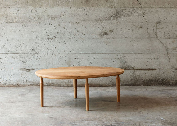A minimalist oblong wooden coffee table with four tapered legs, set against a textured concrete wall and floor.